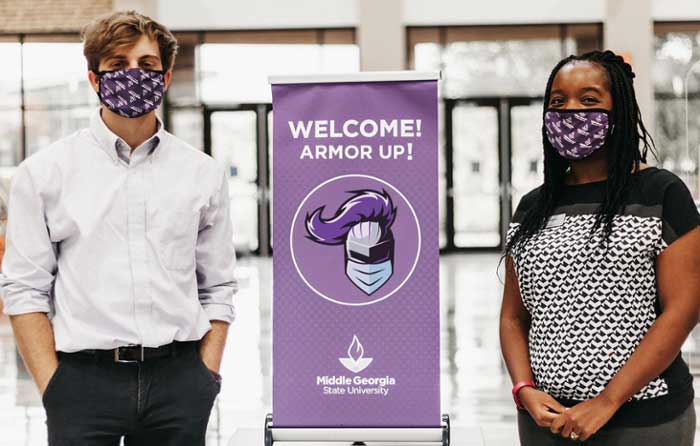 Students wearing masks next to a sign that reads "Welcome! Armor Up!"